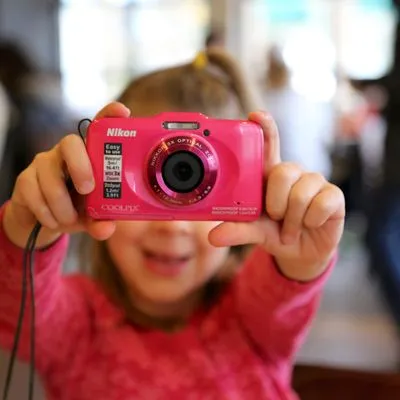 A little girl holding a pink camera in front of her face
