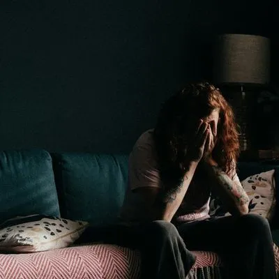 Person sat in dark room on sofa with their head in their hands in despair