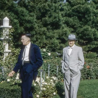 Two men dressed in suits. One is wearing a hat and bow tie. 