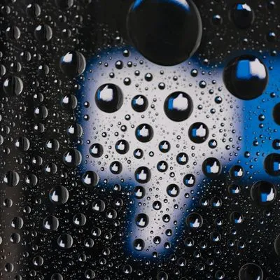 Facebook Like Thumb but pointing downwards, behind glass which is covered in rain droplets each with a like thumb pointing up inside it.