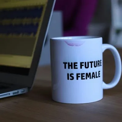 A mug next to a laptop. The mug has text on it readying "the future is female" and has red lipstick on it.