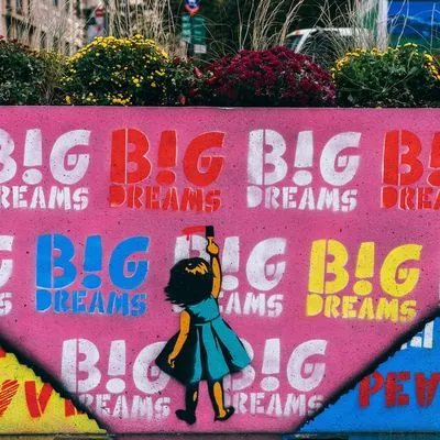 Graffiti on a wall showing a little girl painting the words "Big dreams" over and over.