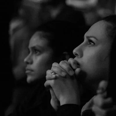 A black and white photo of a women intently listening with her clasped hands resting on her chin.