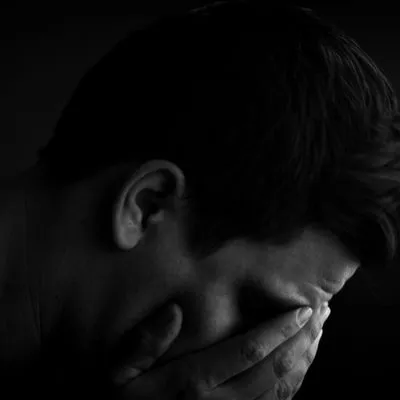 Black and white photo of a man with his head in his hands. Photo by Gabriel Cox on Unsplash