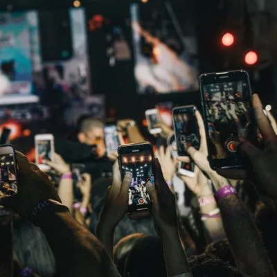 Loads of people in a crowd all filming something on their phones.