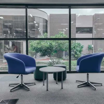 Two empty blue chairs facing each other in an office with a large window behind.