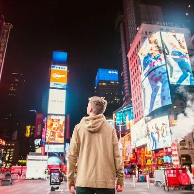 Man standing in front of high-rise buildings and brightly lite billboard adverts in Times Square, New York.