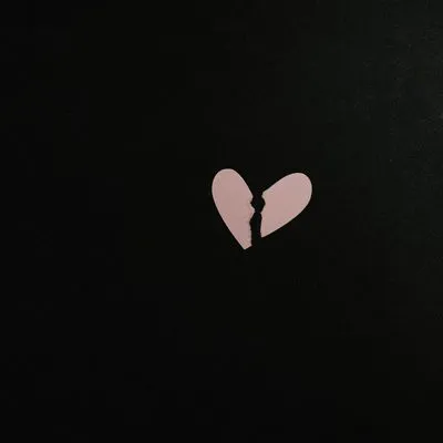 Two pieces of pink paper in the shape of a heart, ripped in two.