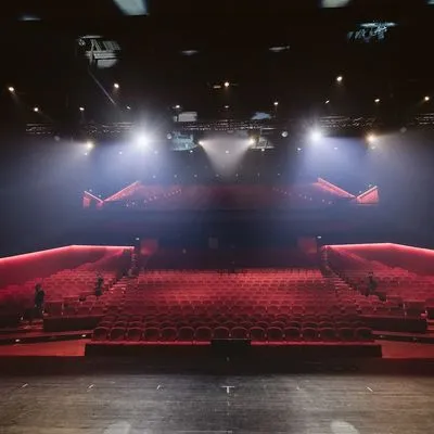 Photo from the perspective of someone standing on a stage with the stage lights on, looking out into an empty auditorium of red seats.