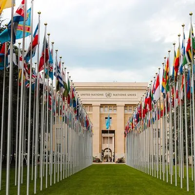A green lawn lined with different flags with the United Nations office building in the background.
