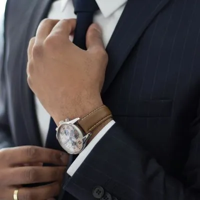 Photo of a man wearing a fancy suit and watch, adjusting his tie.