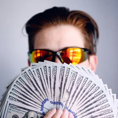 Man with sunglasses on holding a fan of American one hundred dollar bills.