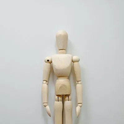 a wooden mannequin standing in front of a white wall