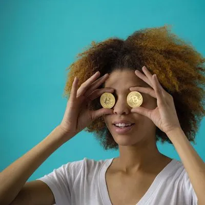 Lady holding coins over her eyes with the bitcoin logo on. 
