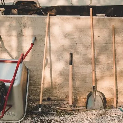 Shovel and a wheelbarrow leading against a brick wall.