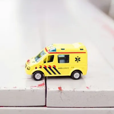 Yellow toy ambulance on a white wooden bench.